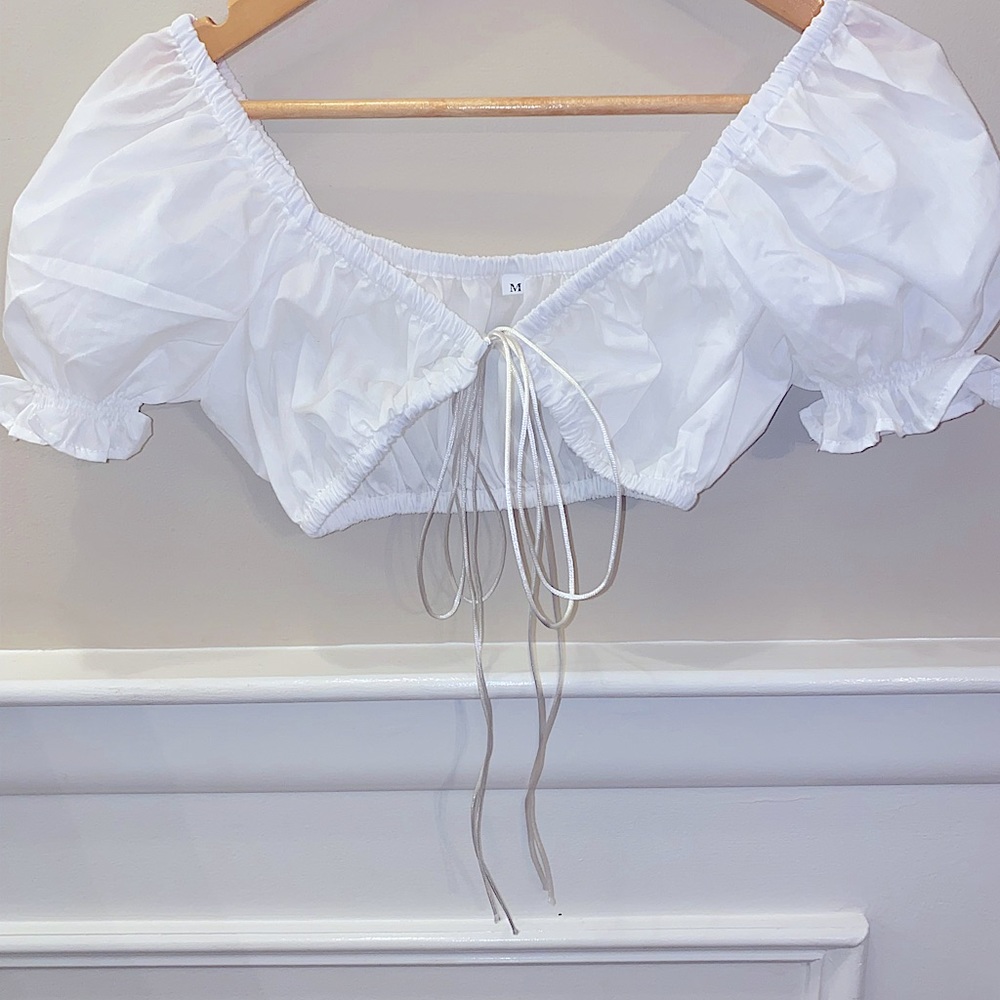 White, cropped, whimsical top with a sweetheart neck and adjustable ties.